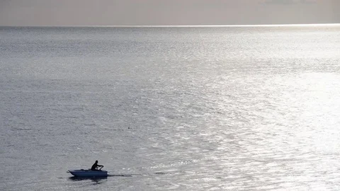 Fisherman rowing with his boat on the flat and shimmering sea Stock Footage 82965914