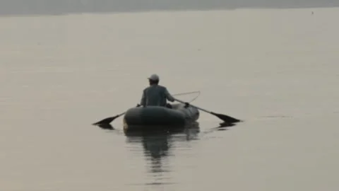 Fisherman rowing an inflatable rubber boat on a wide river Stock Footage 337754368