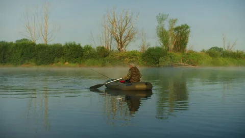 A fisherman is rowing while sitting in a boat in the morning on the lake Stock Footage 251731811