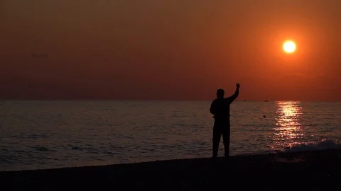 Fisherman silhouette at sunset throws leash in the sea Stock Footage 100451352