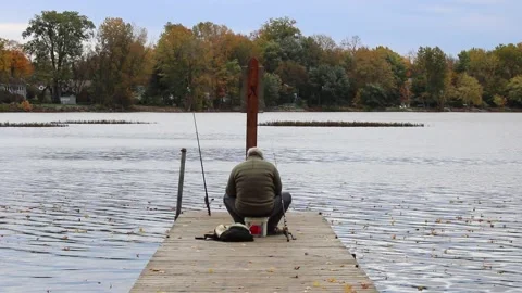 Fisherman sitting on the end of a dock, seen from behind, with his gear Stock-Footage 167672107