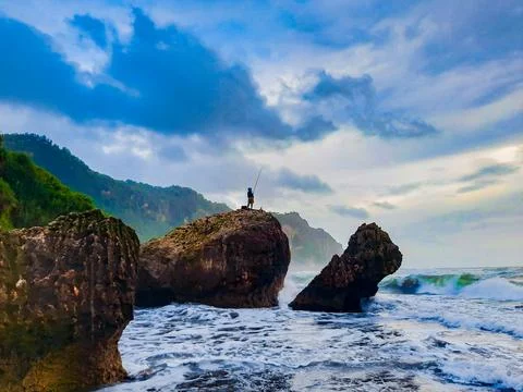 A fisherman sitting on a rock formation while big long waves flowing. Photos