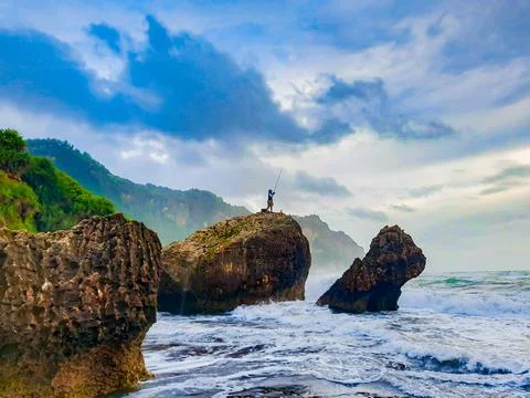 A fisherman sitting on a rock formation while big long waves flowing. Photos