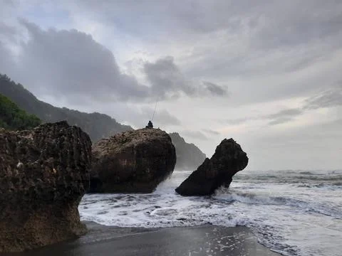 A fisherman sitting on a rock formation while big long waves flowing. A fi... Photos