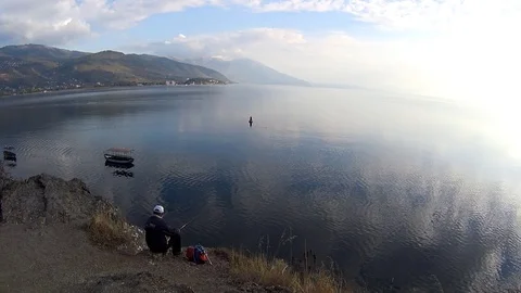 Fisherman sitting on rock while fishing in Lake Ohrid at sunset, Macedonia Stock Footage