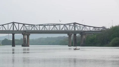 Fisherman in Small Boat Floating on River Near Steel Truss Bridge 스톡 동영상 343590626