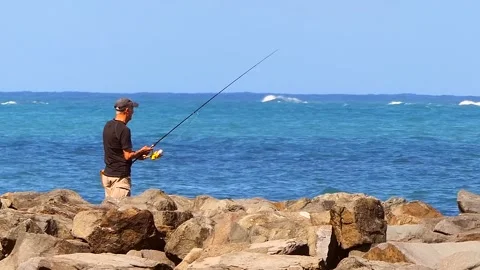 Fisherman Standing on Big Rocks on the Beach Stock Footage 221931096