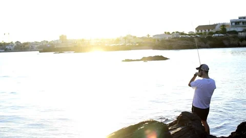 Fisherman standing at the seashore hooks a fish against sunset Vídeos de archivo 130894850