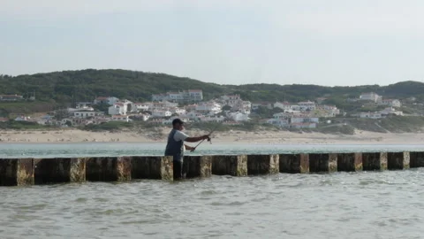 Fisherman Throwing Hook From Pier Over Calm Sea With Coastal Village Video stock 338331305