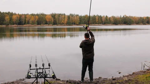 Fisherman using spod rod to feed fish in calm autumn lake, man in jacket and Video stock 319662826