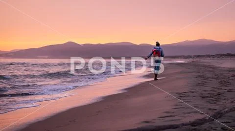 Fisherman walking on the shore at sunset Stock Photos