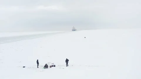 Fishermen catch the fish on ice covered water near fireway, ships on background Stock Footage 170385241