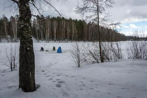 Fishermen on the ice of a small river on a cloudy spring day. Stock Photos