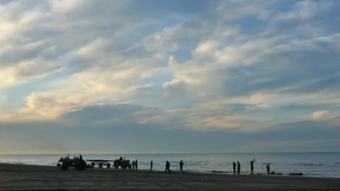 Fishermen prepare nets on the beach at dawn, with tractors silhouetted Stock Footage 317910708
