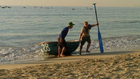 Fishermen pull traditional round basket bamboo boat up along shore at Stock Footage 250765486