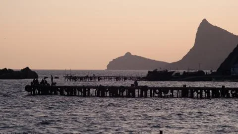 Fishermen sit on the dock and catch fish at sunset Stock Photos
