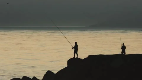 Fishermen stand on rocks and fish in the sea at late sunset Stock Footage 255041899