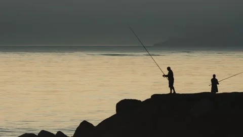 Fishermen stand on rocks and fish in the sea at sunset Stock Footage 255041902