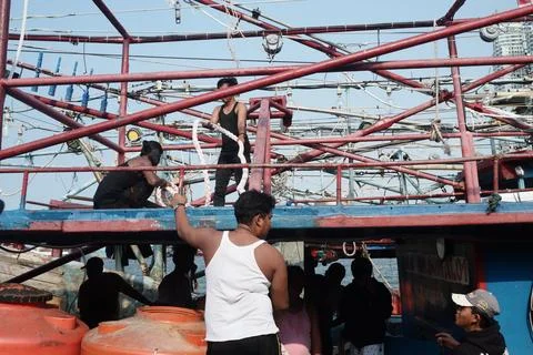 Fishermen work rigging aboard boat at busy harbor Stock Photos
