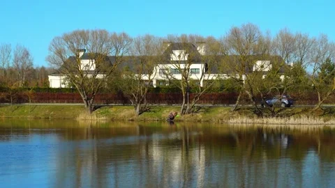 Fishing along a calm lake near a large house in a quiet neighborhood on a sunny Stock Footage 337525053