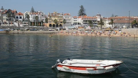 Fishing boat on foreground with crowded sandy beach in Cascais near Lisbon Stock Footage 94003077