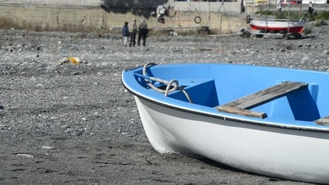 A fishing boat left on the beach while people walk Stock Footage 88038789