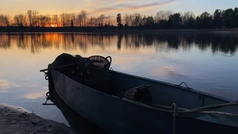 A fishing boat with nets and baskets rests by the shore at sunset, capturing the Stock Footage 305445410