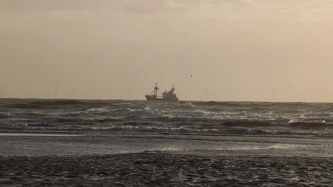A fishing boat sails through rough ocean waves under a hazy sky Wind turbin Stock Footage 304671699