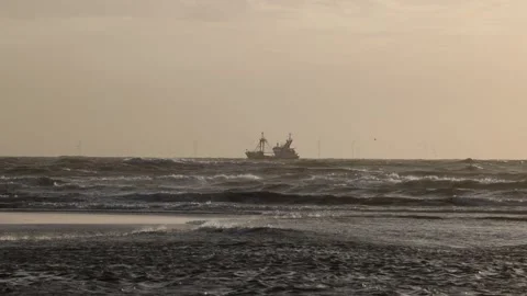 A fishing boat sails through rough ocean waves under a hazy sky Wind turbines Stockbeeldmateriaal 305245408