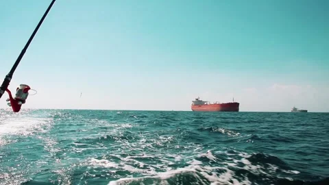 Fishing from a boat while passing a large red cargo ship on the open sea Stock Footage 312039056