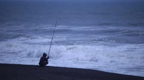 Fishing on a Cloudy Beach with Rough Waves Stock Photos