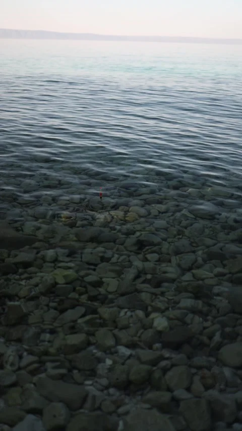 Fishing float and spinning rod waiting above clear calm water Stockbeeldmateriaal 341321305