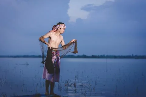 Fishing man use throwing net to catch fish in lake at sunset 스톡 사진