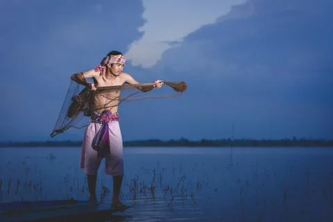 Fishing man use throwing net to catch fish in lake at sunset Stockfoto's