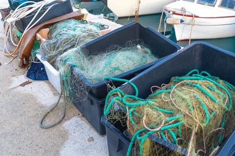 Fishing nets in black boxes by harbor with boats in background Stock Photos
