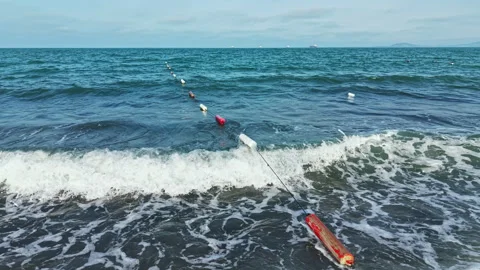 Fishing nets float on the ocean surface near the shore while gentle waves roll Stock Footage 337913218