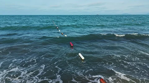 Fishing nets float in the water near the shore as waves crash under a clear sky Stock Footage 337889598