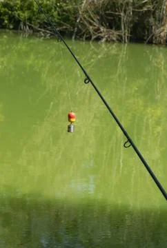 Fishing rod with float and feeder hanging above calm green pond water in qu.. Stock Photos