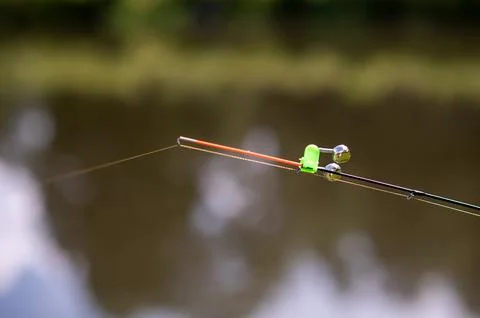 Fishing rod tip with bell bite alarm on blurred water background.. Stock Photos