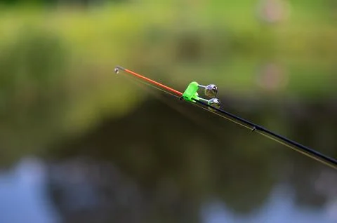Fishing rod tip with bell bite alarm on blurred water background.. Stock Photos