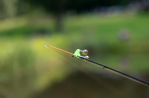 Fishing rod tip with bell bite alarm on blurred water background.. Stock Photos