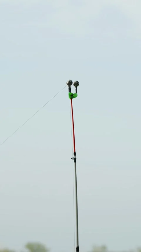 Fishing rod tip with green bite alarm bells against sky Stock Footage 337753167