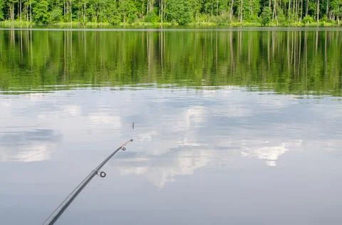 Fishing rod, water surface, float, day, reflection of clouds. Stock Photos