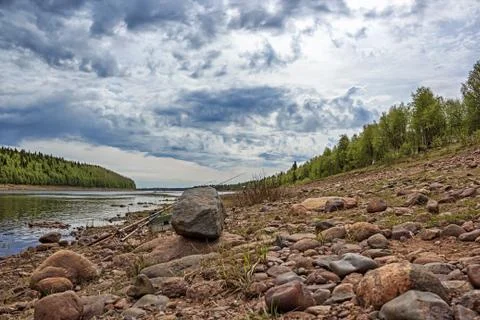 Fishing rods in the composition with a stone at the river under a cloudy sky Foto stock