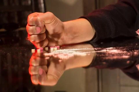 A fist knocking on a table from which tablets and narcotic substances scatter Stock Photos