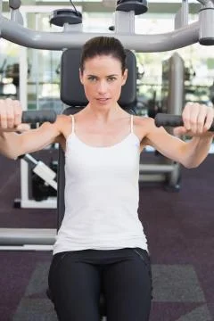 Fit brunette smiling at camera using weights machine for arms 스톡 사진