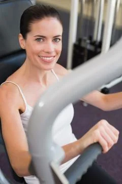 Fit brunette using weights machine for arms smiling at camera 스톡 사진