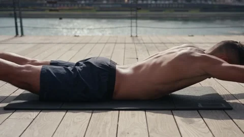 A fit caucasian man does Superman Back Extensions on a black mat. Isometric Stock Footage 218204041