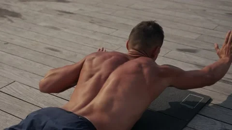 A fit caucasian man does Superman Back Extensions on a black mat. Isometric Vidéo 218204434