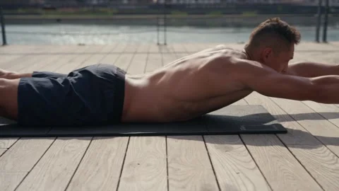 A fit caucasian man does Superman Back Extensions on a black mat. Isometric Stock Footage 218477913